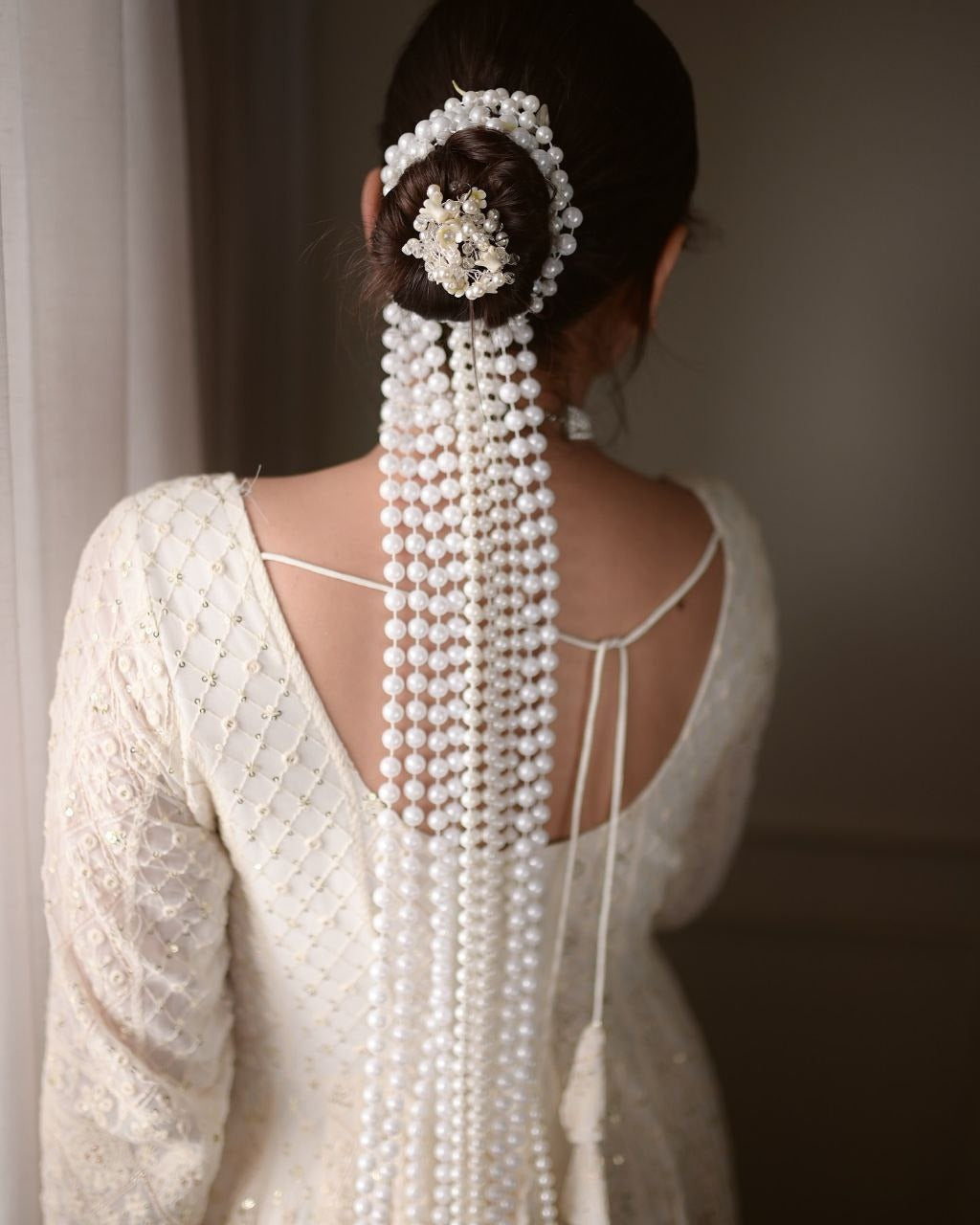 Woman wearing a white beaded hairpiece with long strands cascading down her back.