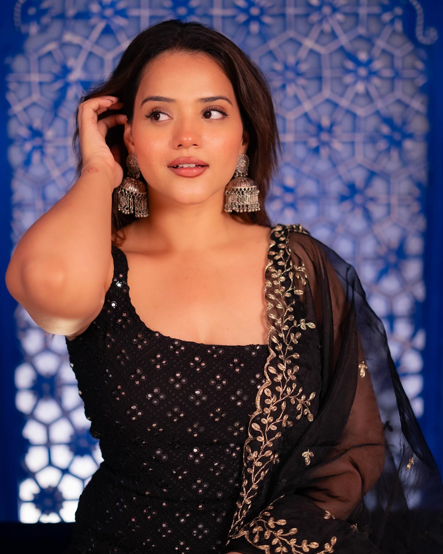 Woman wearing a black traditional outfit with gold embroidery against a blue patterned background