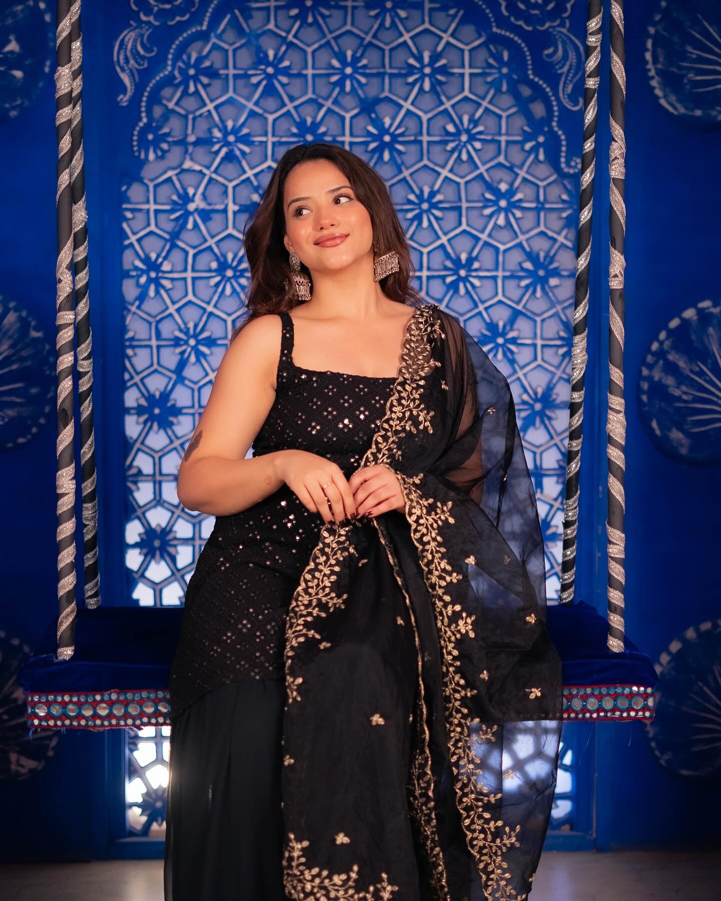 Woman in a black and gold traditional outfit against a blue decorative wall.