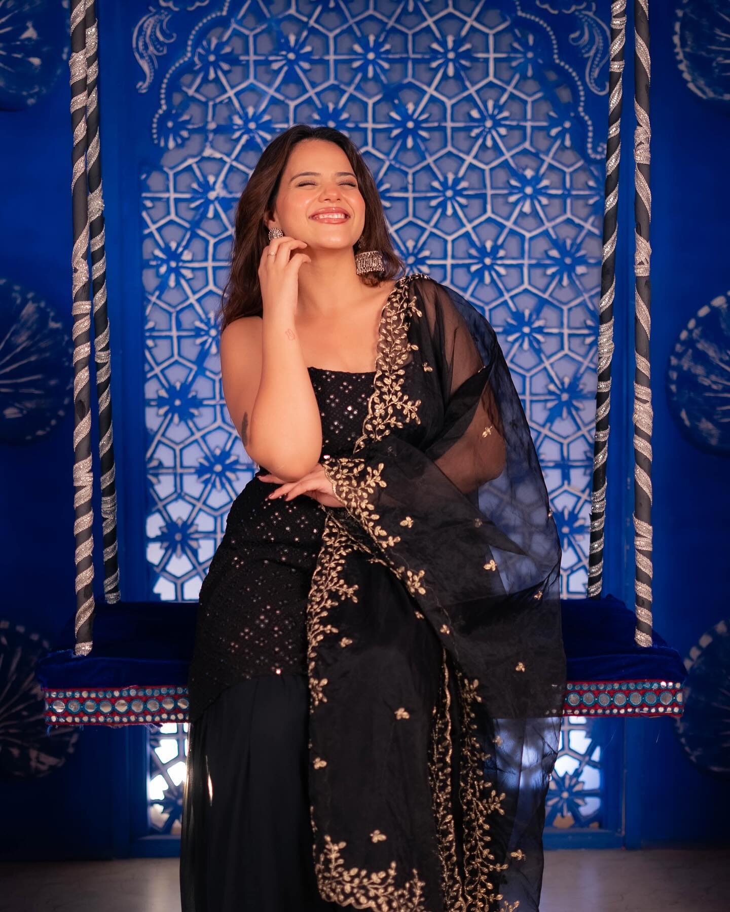 Woman in a black and gold outfit posing against a blue decorative backdrop