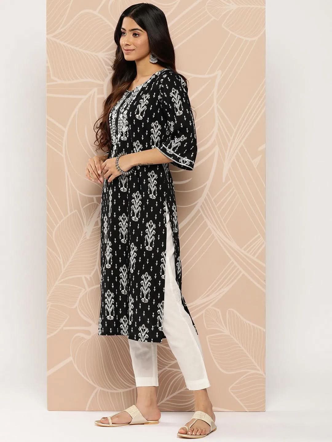Woman wearing a black and white patterned kurta with white pants against a beige background