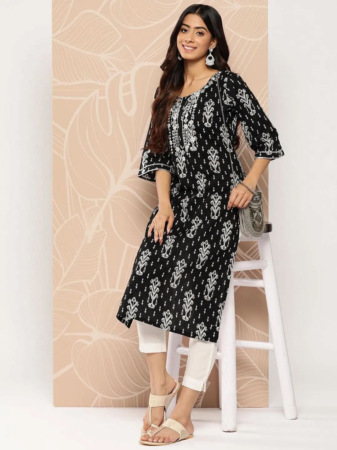 Woman wearing a black and white patterned kurta with white pants against a beige wall.