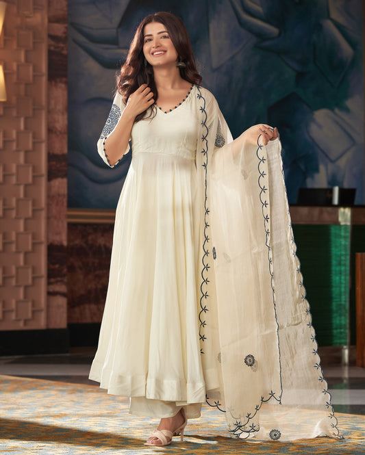 Woman in a white traditional outfit with black embroidery standing indoors.