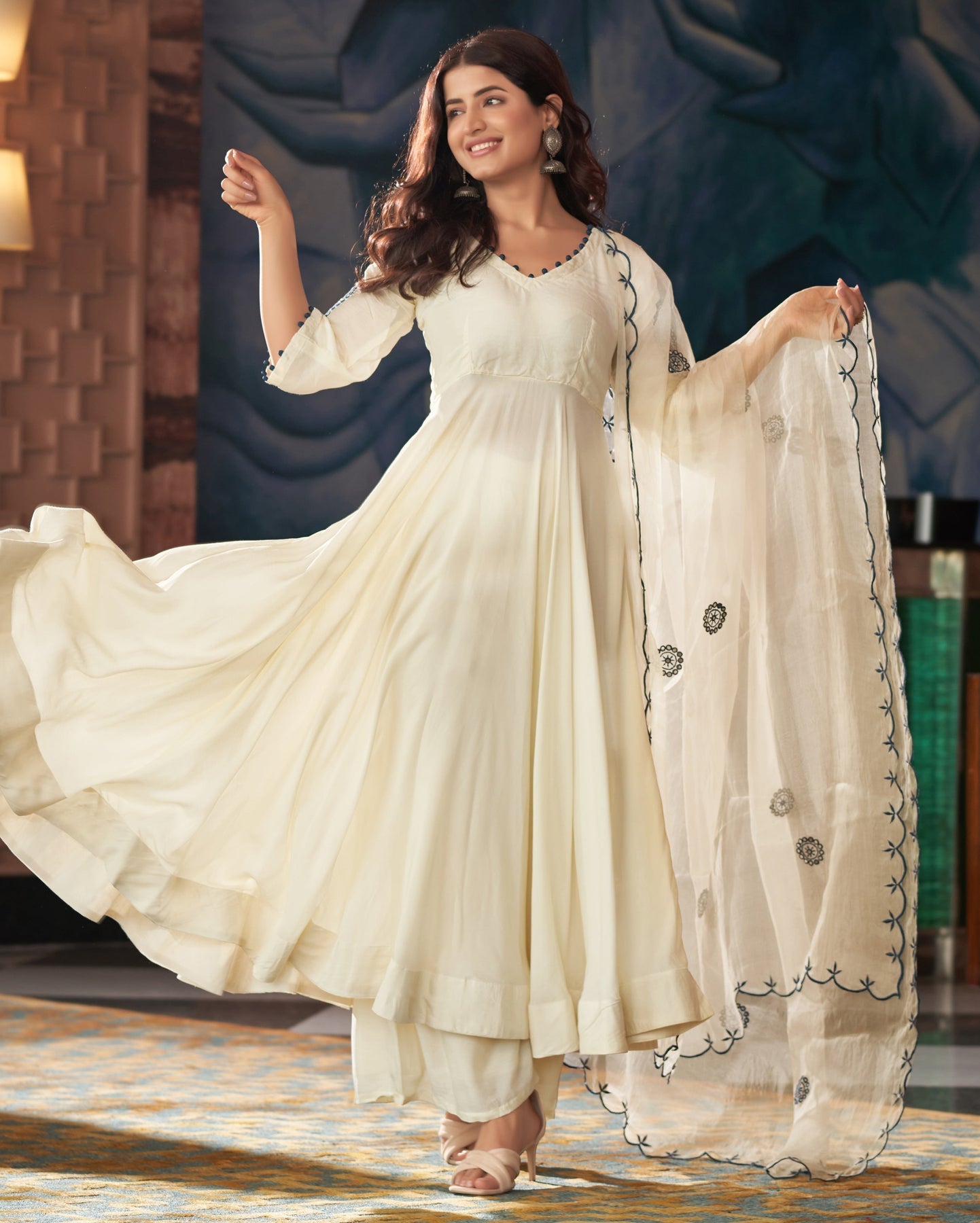 Woman in a white traditional outfit with a matching dupatta, standing indoors.