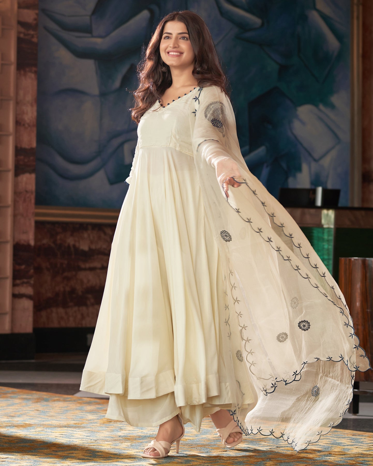 Woman in a cream-colored traditional outfit with a decorative dupatta on a stage.