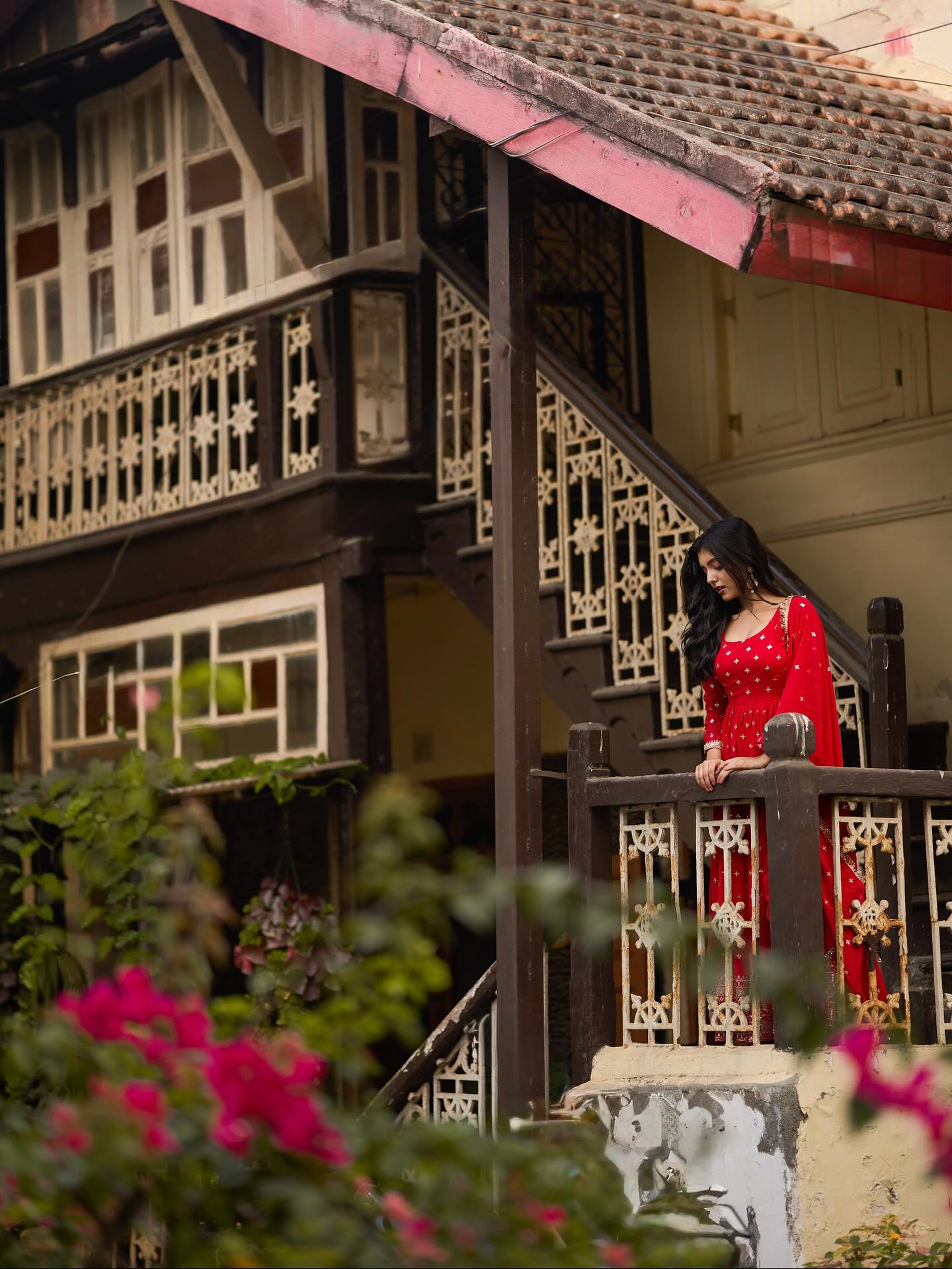 Woman in a red dress standing on a staircase of a traditional house with flowers in the foreground