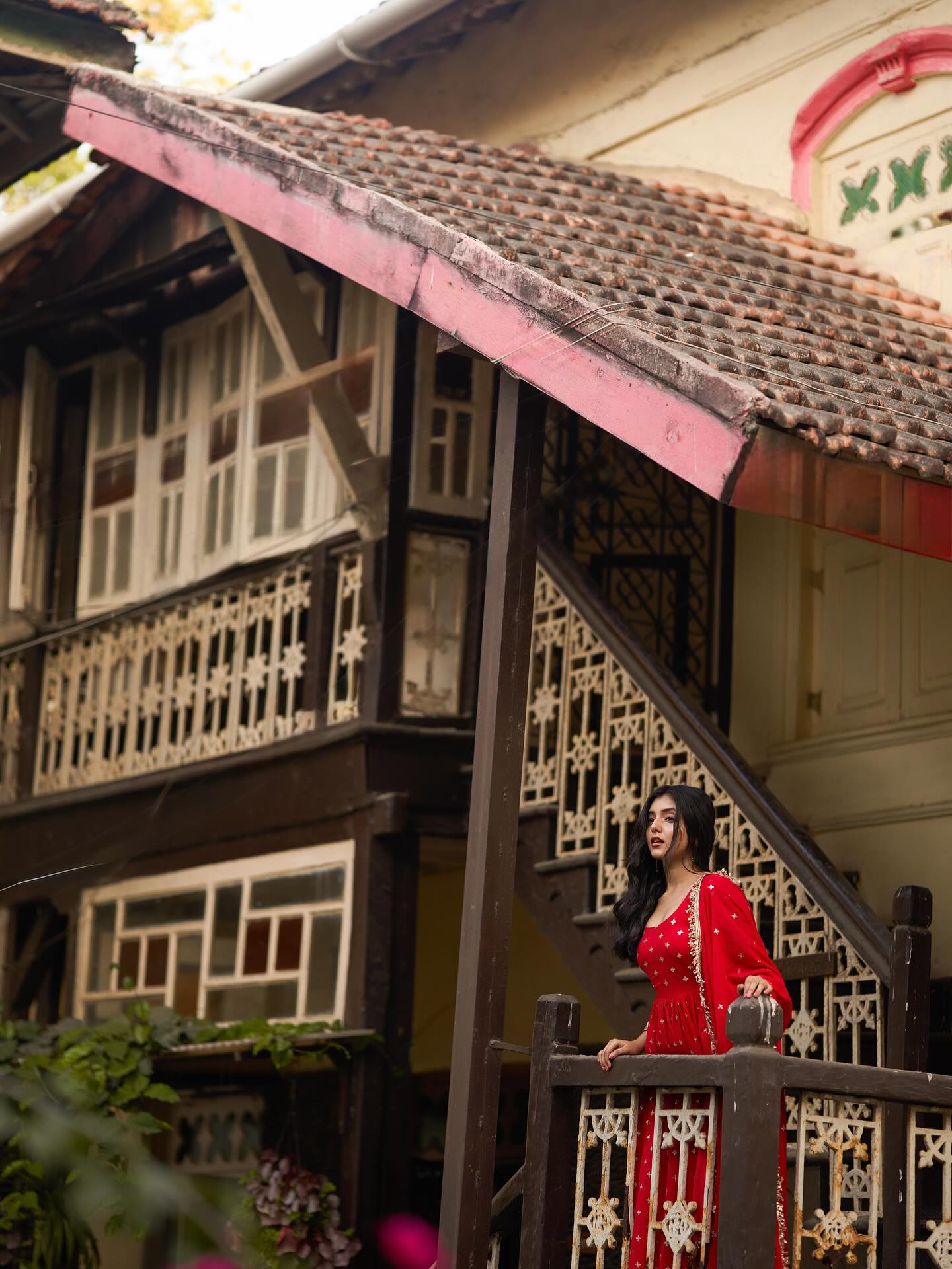 Woman in a red dress standing on a balcony of a traditional house with wooden architecture.
