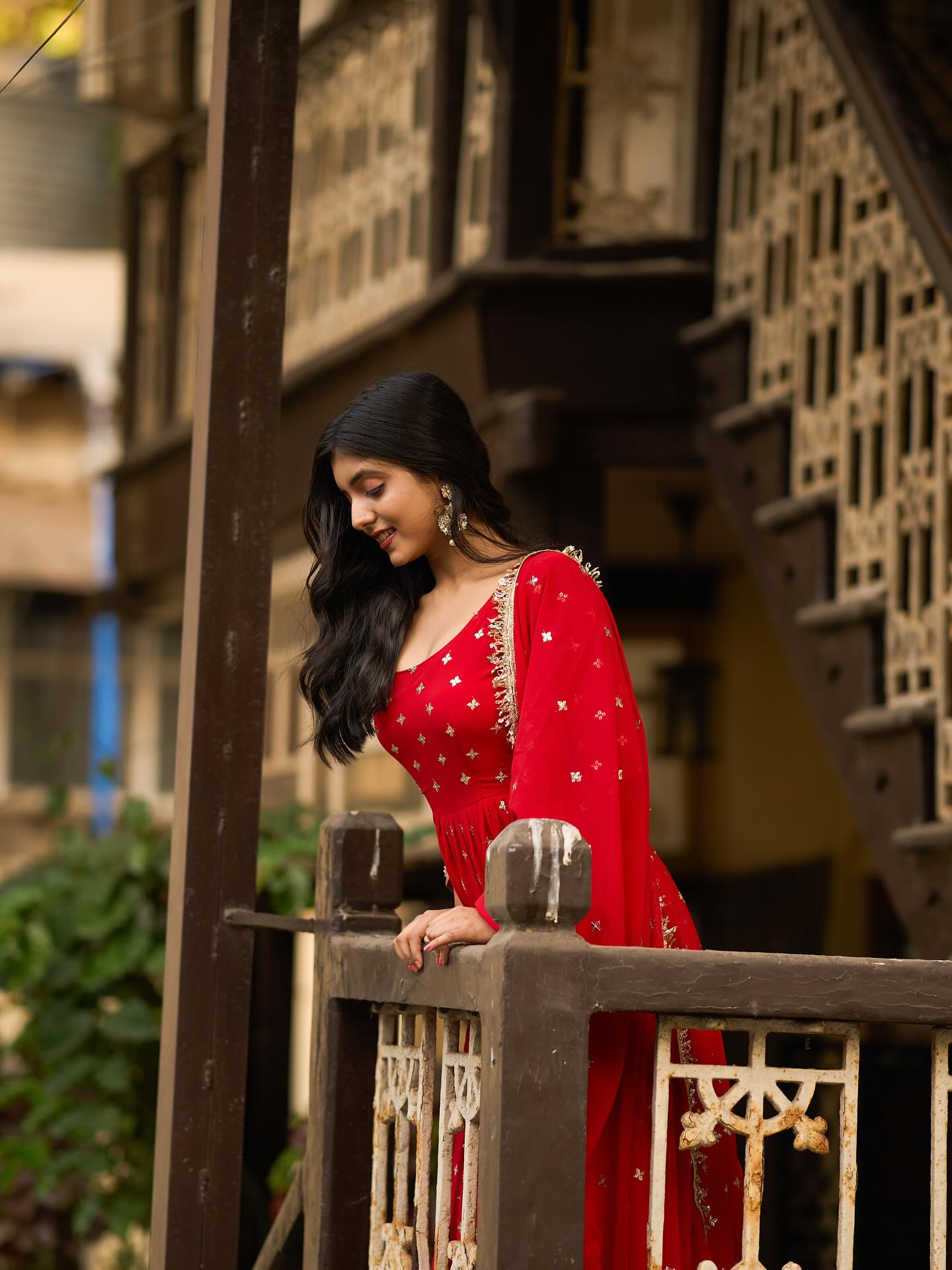 Woman in a red traditional outfit standing on a wooden staircase with a blurred background