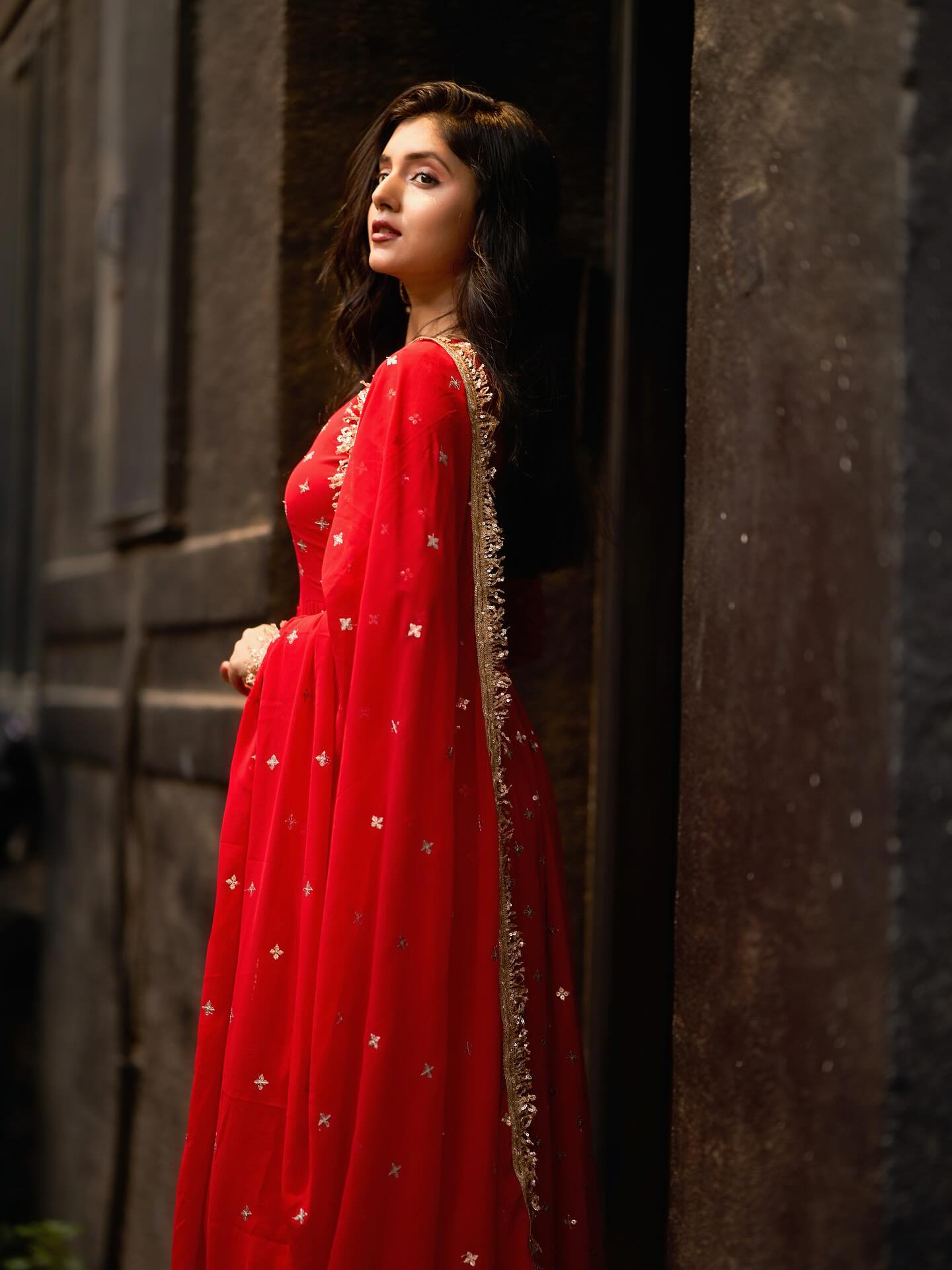 Woman in a red traditional outfit standing against a dark wall.