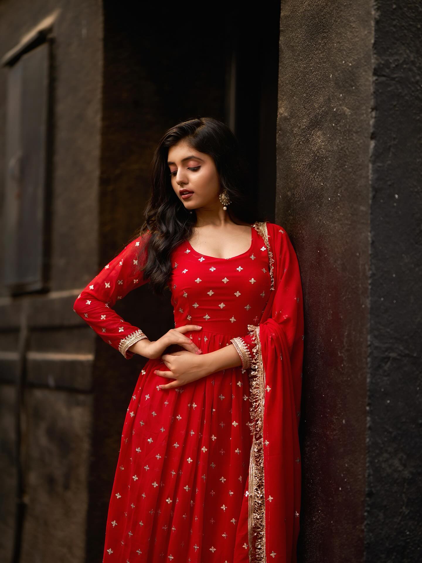 Woman in a red traditional outfit standing against a dark wall.