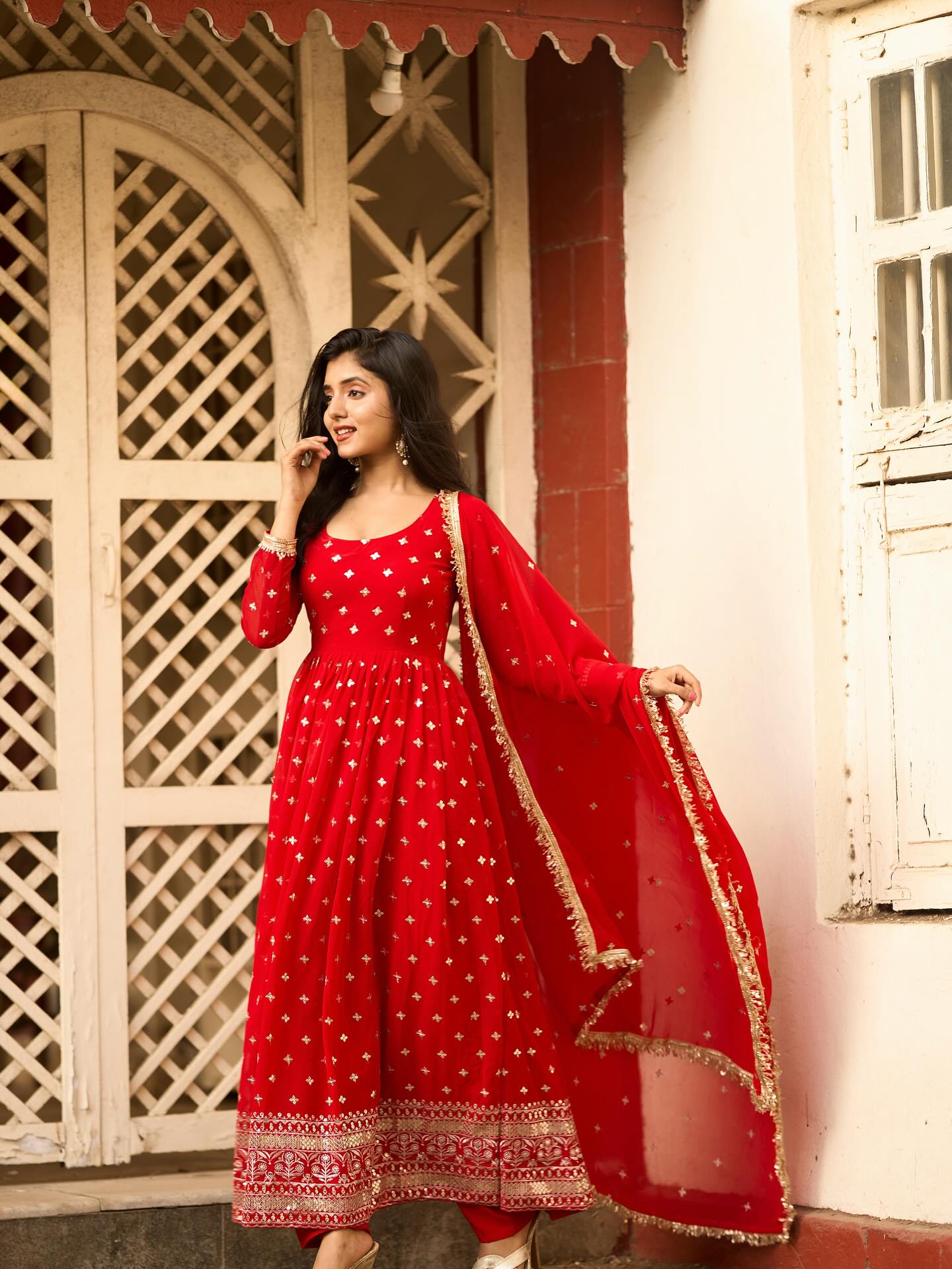 Woman in a red traditional outfit standing in front of a decorative wall.