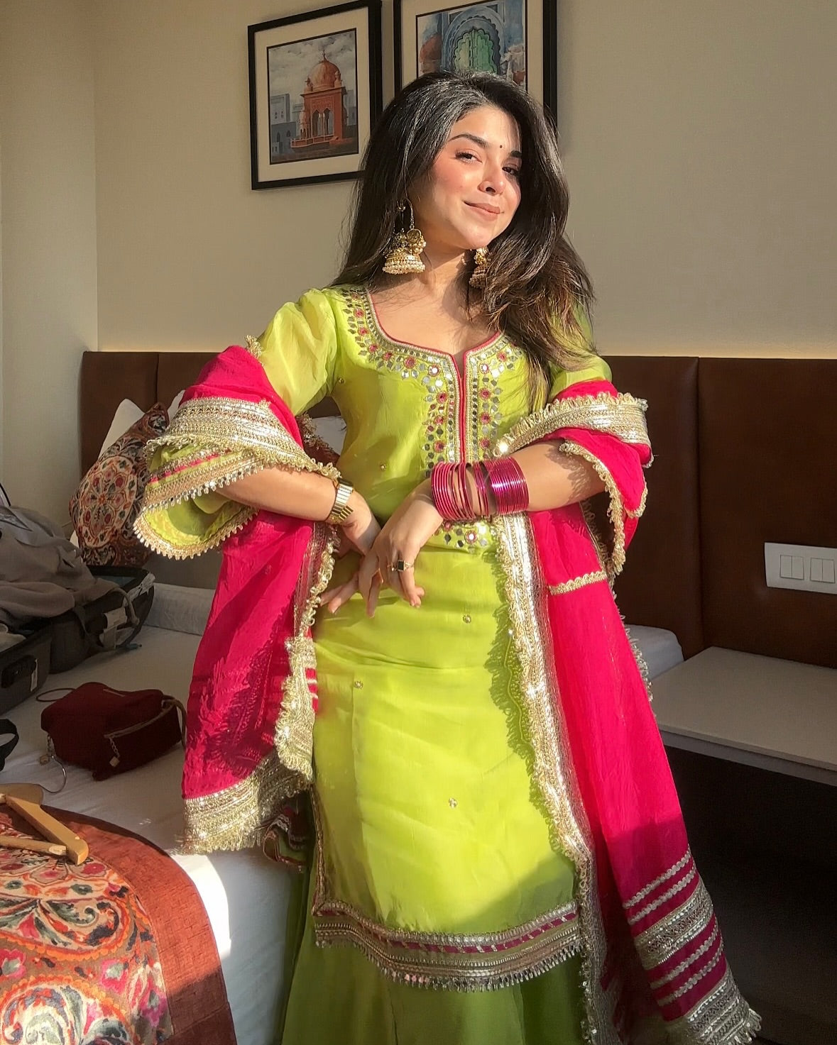 Woman in a green and pink traditional outfit with intricate designs, standing indoors.