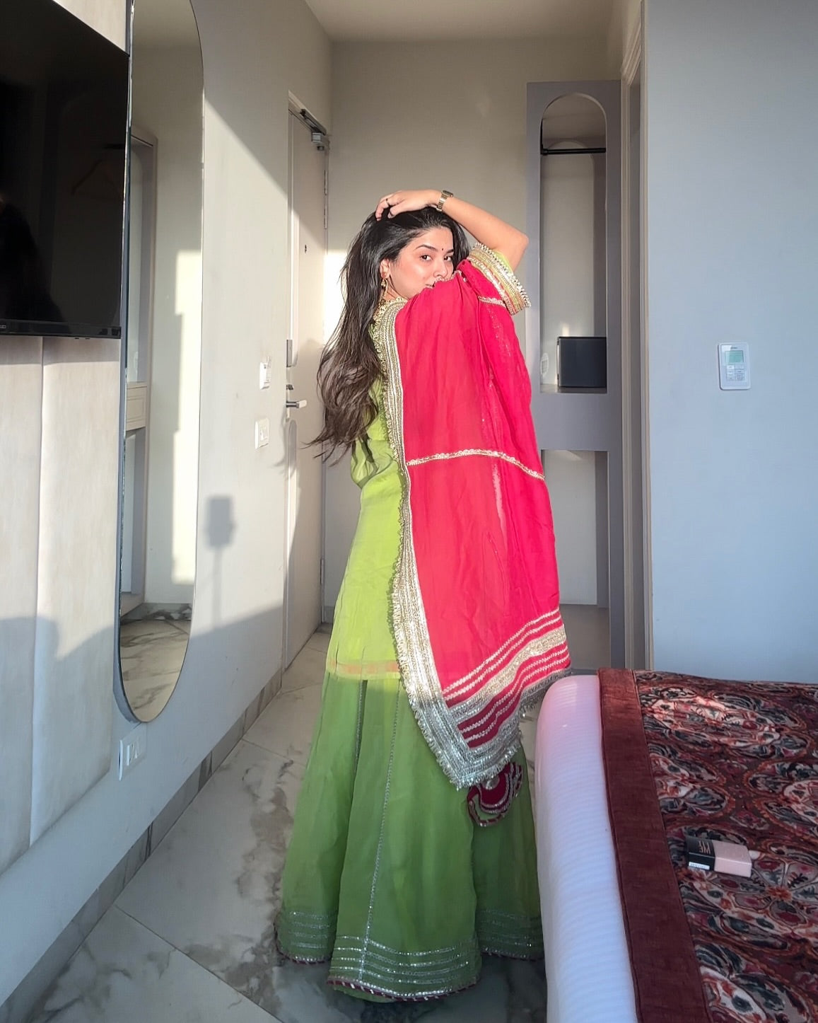 Woman in a green traditional outfit with a pink dupatta standing in a room.