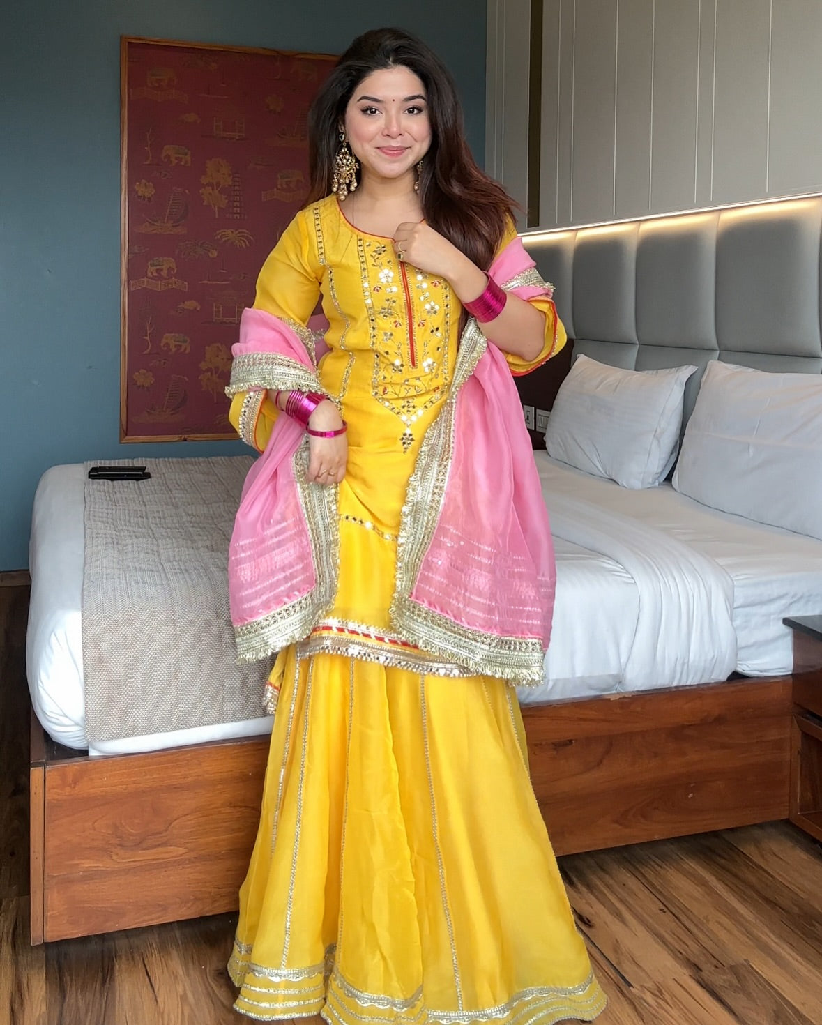 Woman in a yellow and pink traditional outfit standing in a bedroom.