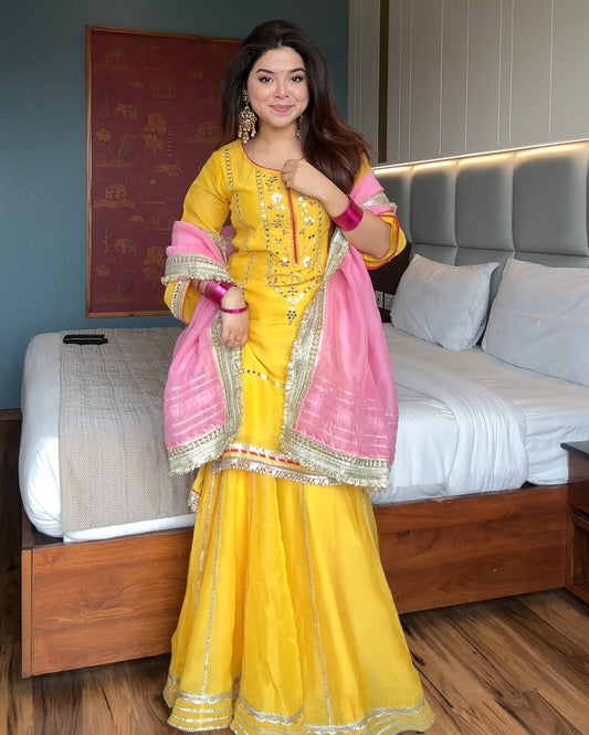 Woman in a yellow and pink traditional outfit standing in a bedroom.