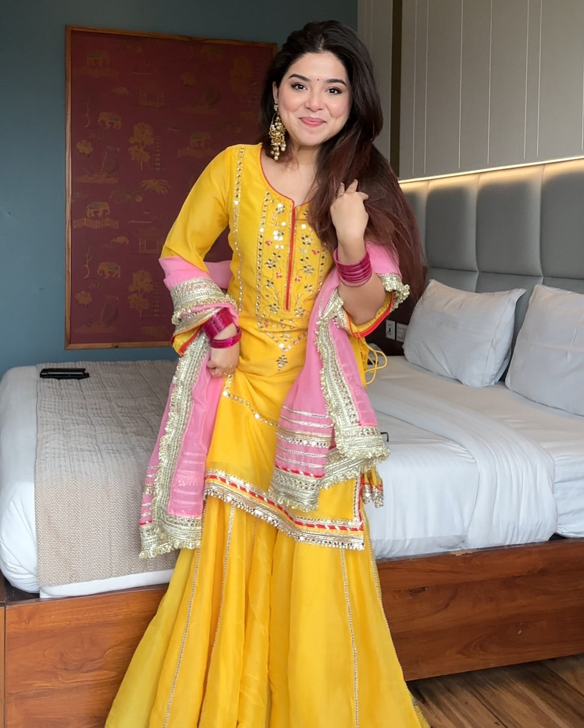 Woman in a yellow and pink traditional outfit standing in a bedroom.