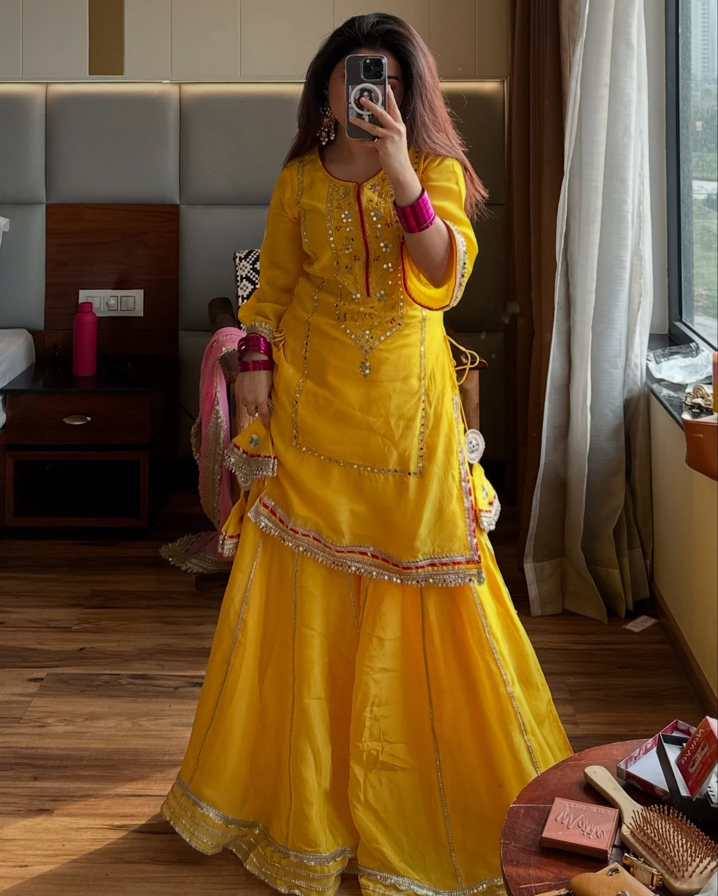 Woman in a yellow traditional outfit taking a mirror selfie in a room.