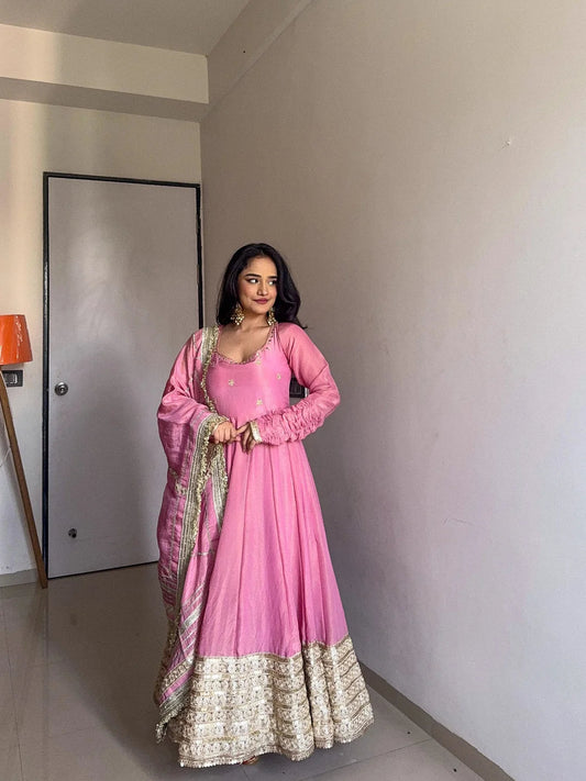 Woman in a pink traditional outfit standing in a room with a neutral wall and door.