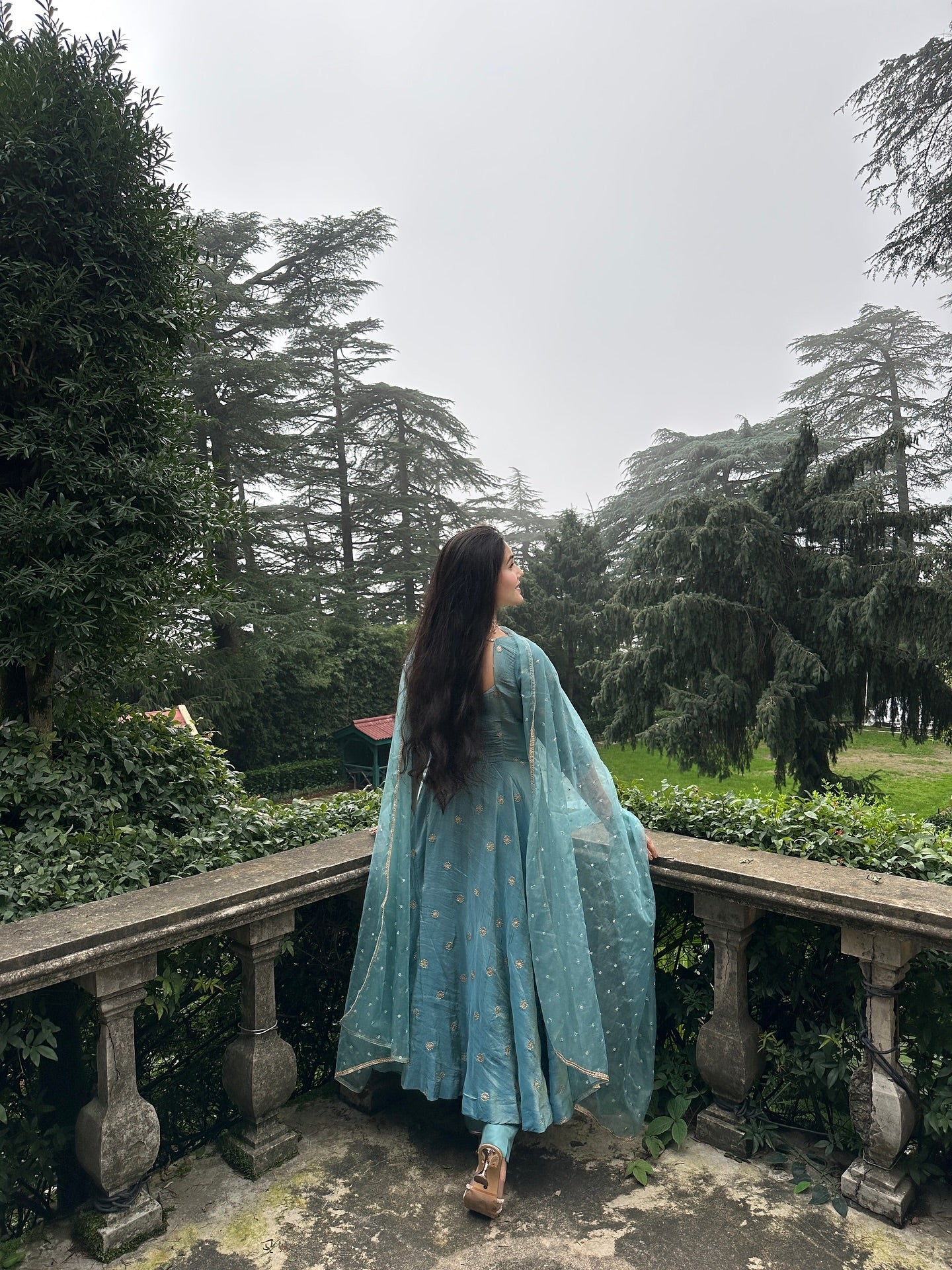 Woman in a light blue dress standing on a stone path with trees in the background