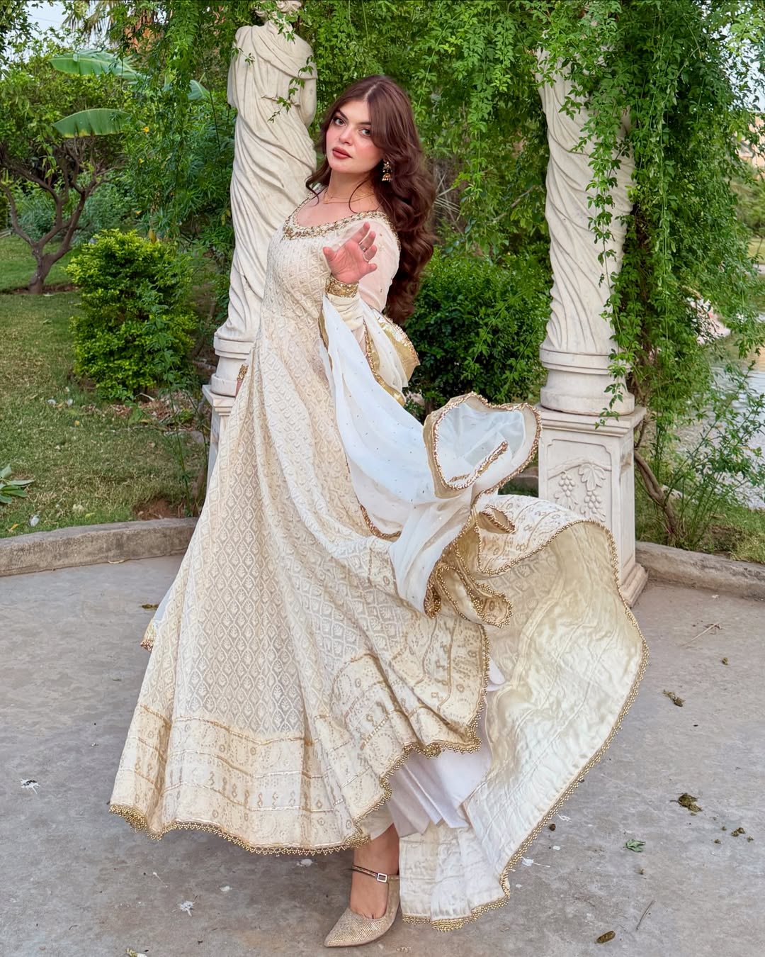 Woman in a traditional outfit standing outdoors with greenery in the background