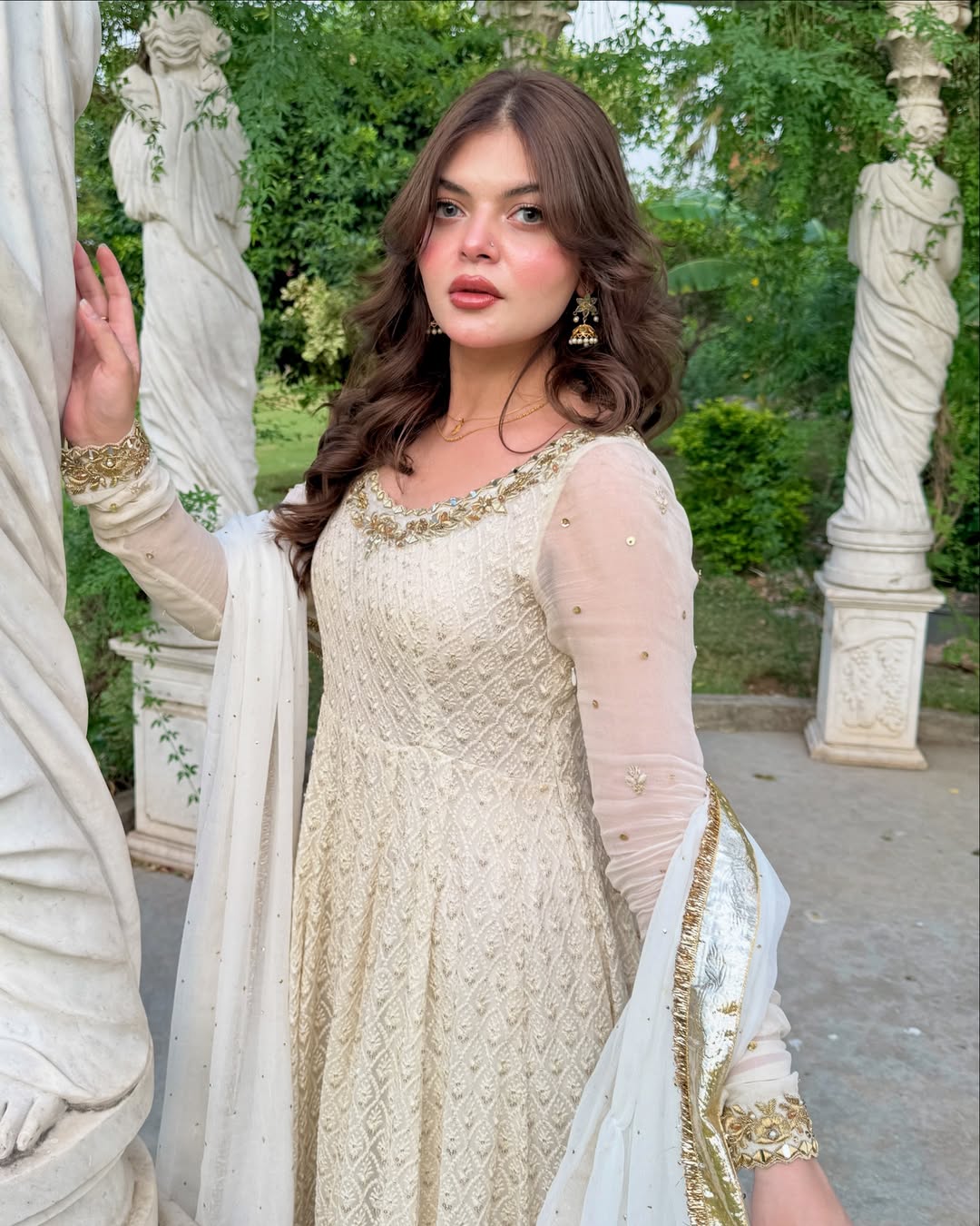 Woman in a traditional outfit standing in an outdoor setting with classical architecture.