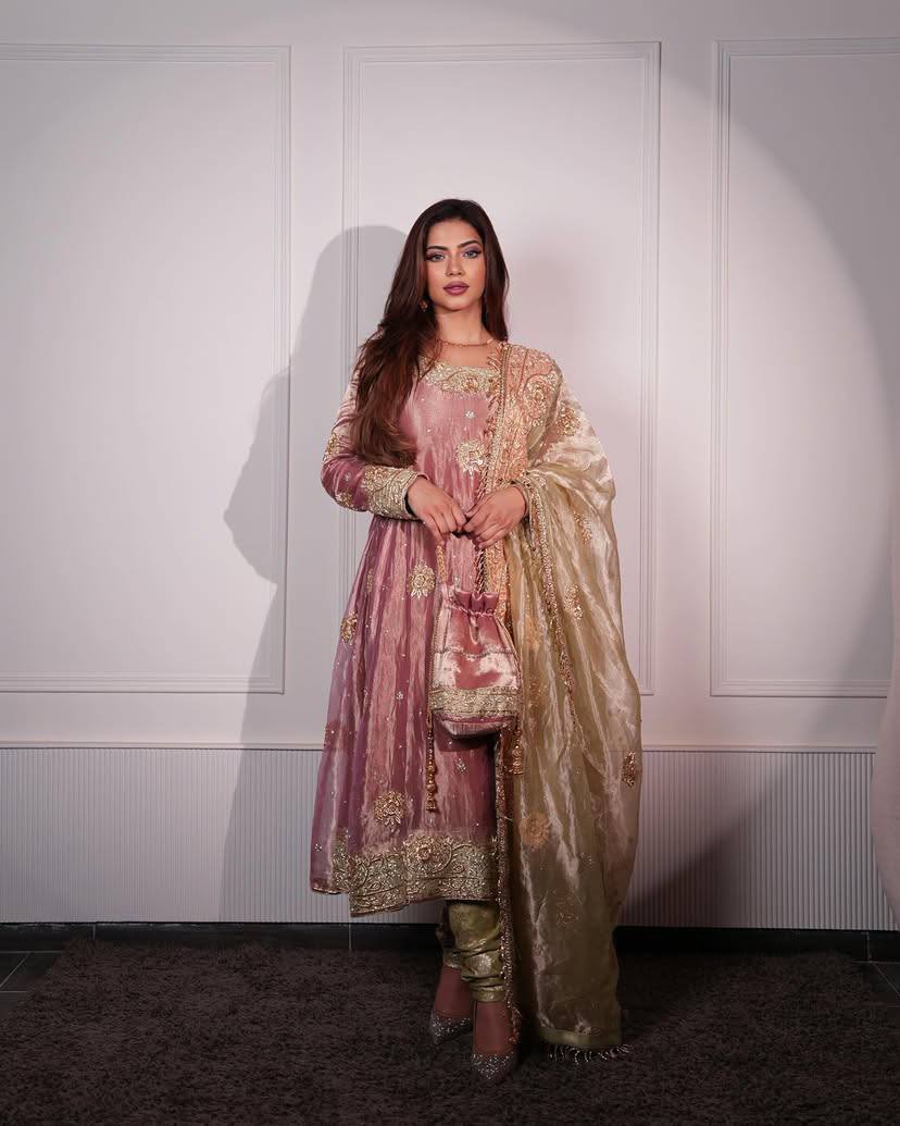 Woman in traditional pink and gold outfit with dupatta against a white wall
