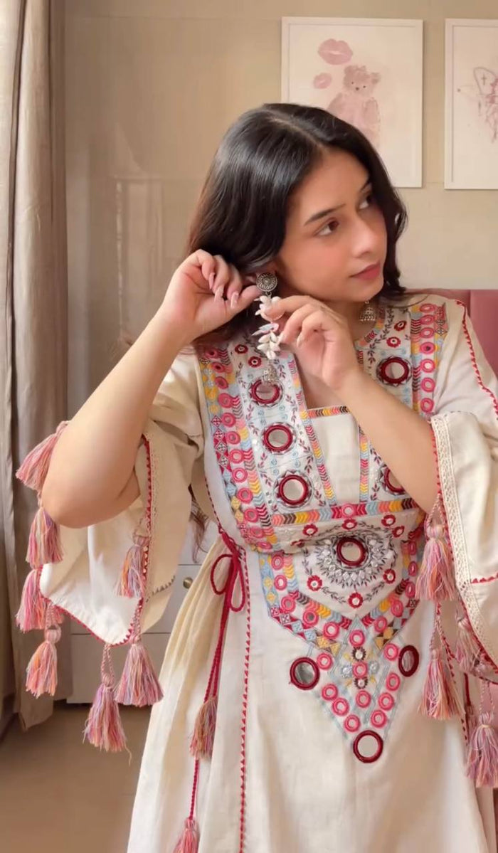 Woman wearing a traditional embroidered outfit with tassels indoors.