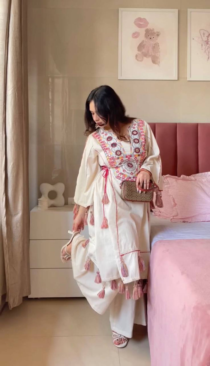 Woman in a white embroidered outfit standing in a bedroom with pink bedding.