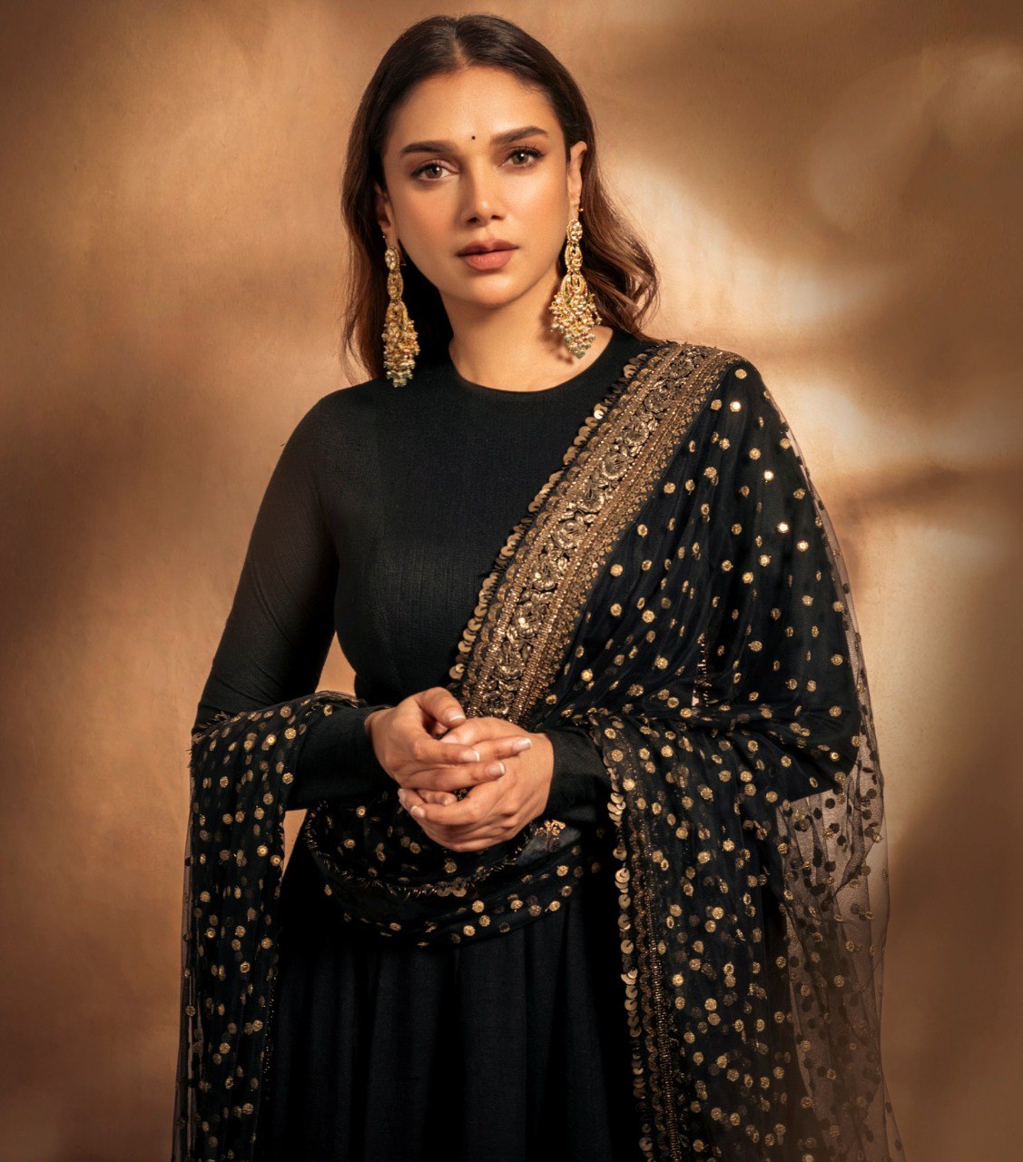 Woman wearing a black outfit with gold embroidery against a warm brown background