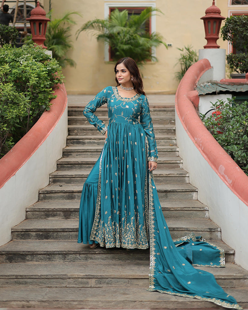 Woman in a blue traditional outfit standing on outdoor steps with greenery.