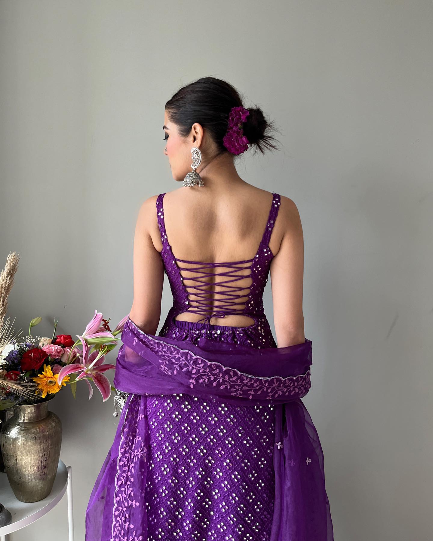 Woman wearing a purple dress with intricate back design, standing against a plain background.
