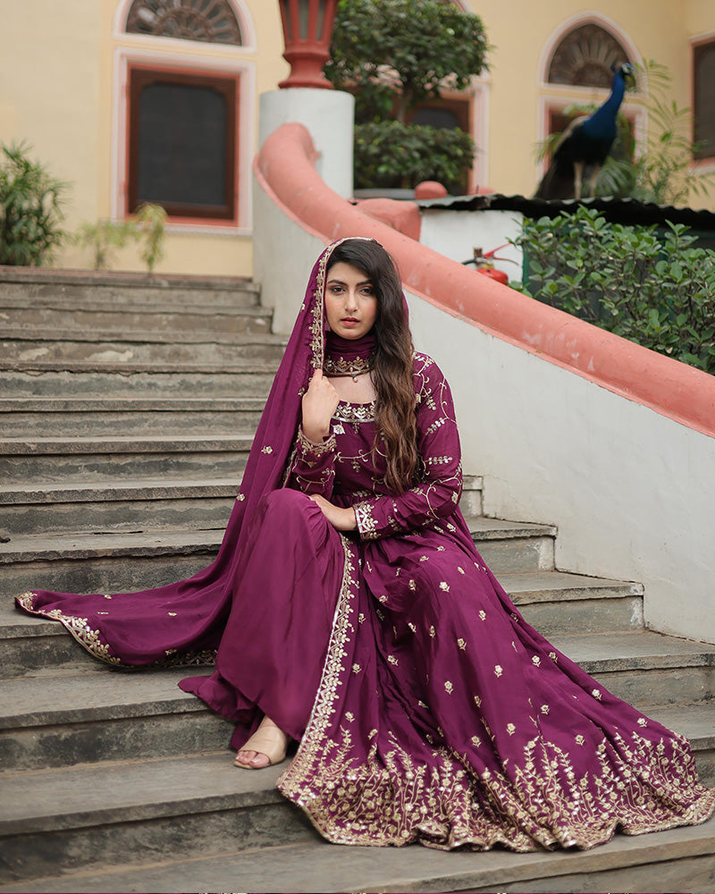 Woman in a traditional purple outfit sitting on steps with a peacock in the background