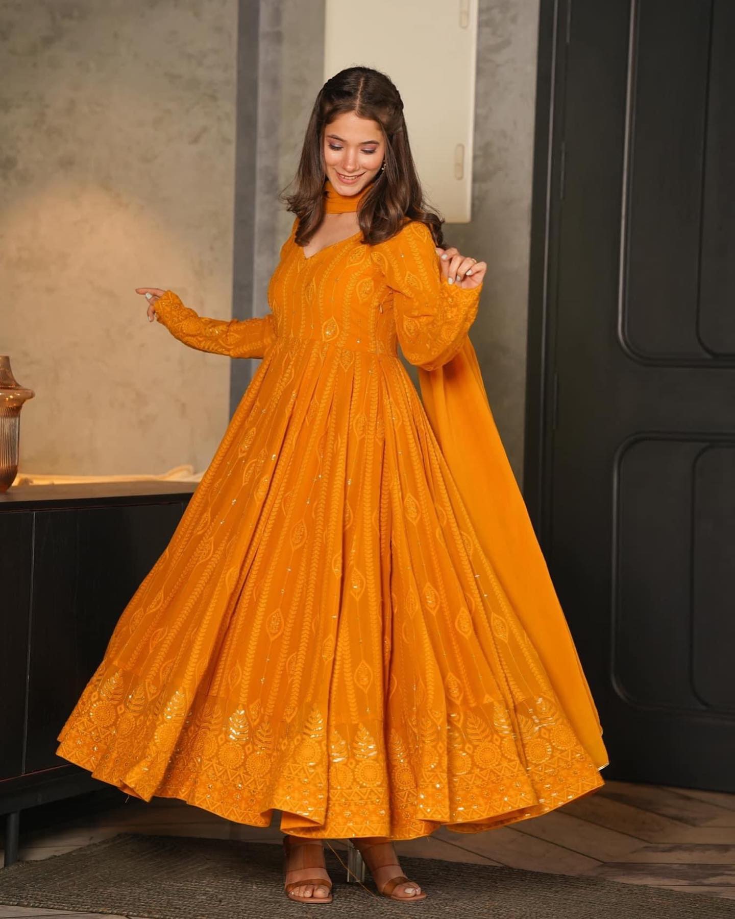 Woman wearing a mustard yellow dress with intricate patterns indoors.