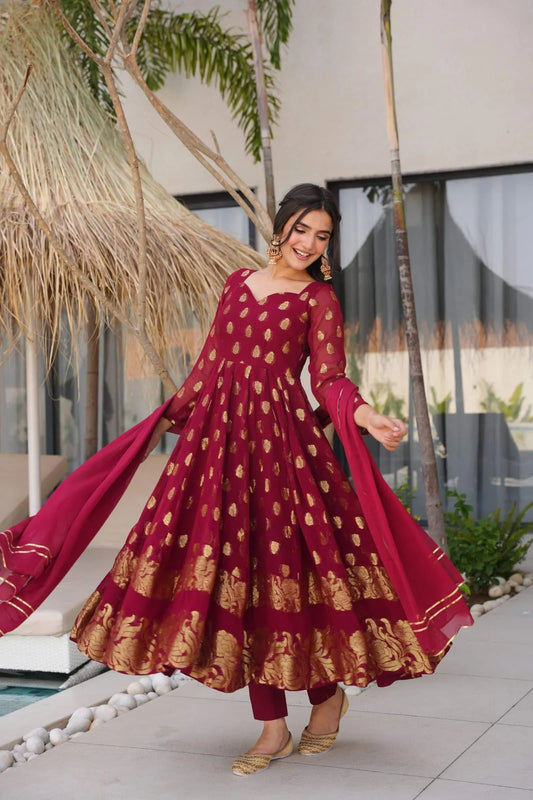 Woman in a red and gold traditional outfit standing outdoors with modern building and palm trees in the background.