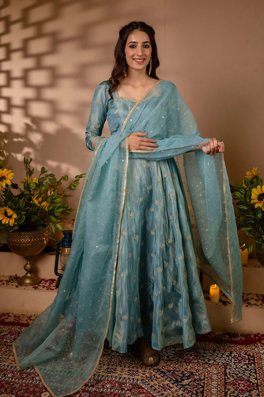 Woman in a light blue traditional outfit standing in a decorated room with flowers and candles.