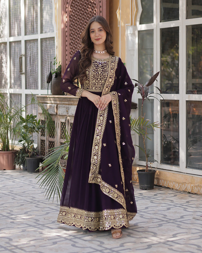 Woman in a dark purple traditional outfit with gold embroidery standing outdoors.