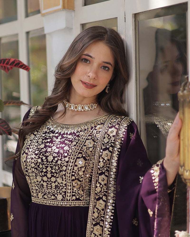 Woman wearing a traditional embroidered outfit with gold and purple colors, holding a decorative item.