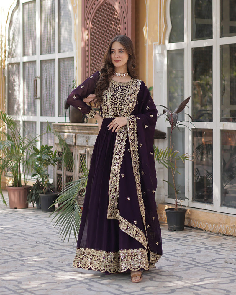 Woman in a dark purple traditional outfit with gold embroidery standing in front of a decorative archway.