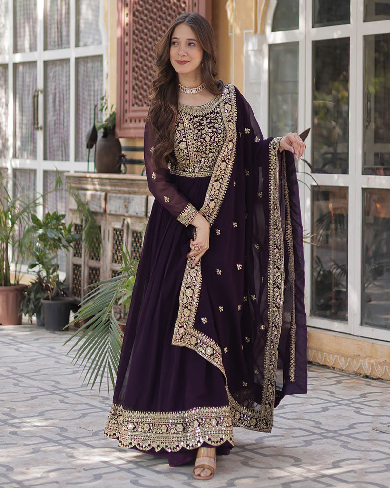 Woman in a dark purple traditional outfit with gold embroidery standing outdoors.