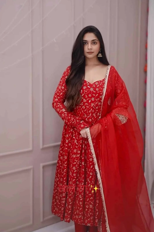 Woman wearing a red traditional outfit with a floral pattern against a neutral background