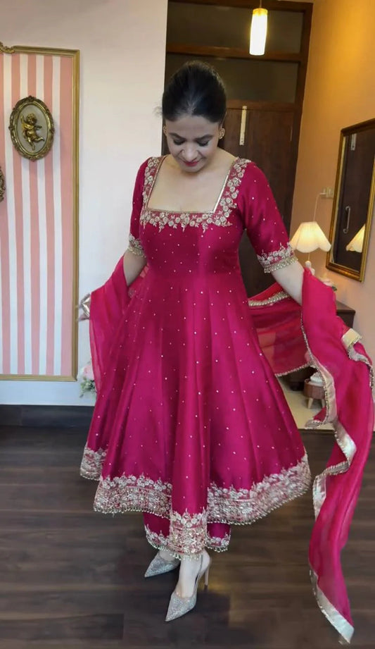 Woman in a pink traditional outfit with white embroidery in a room.