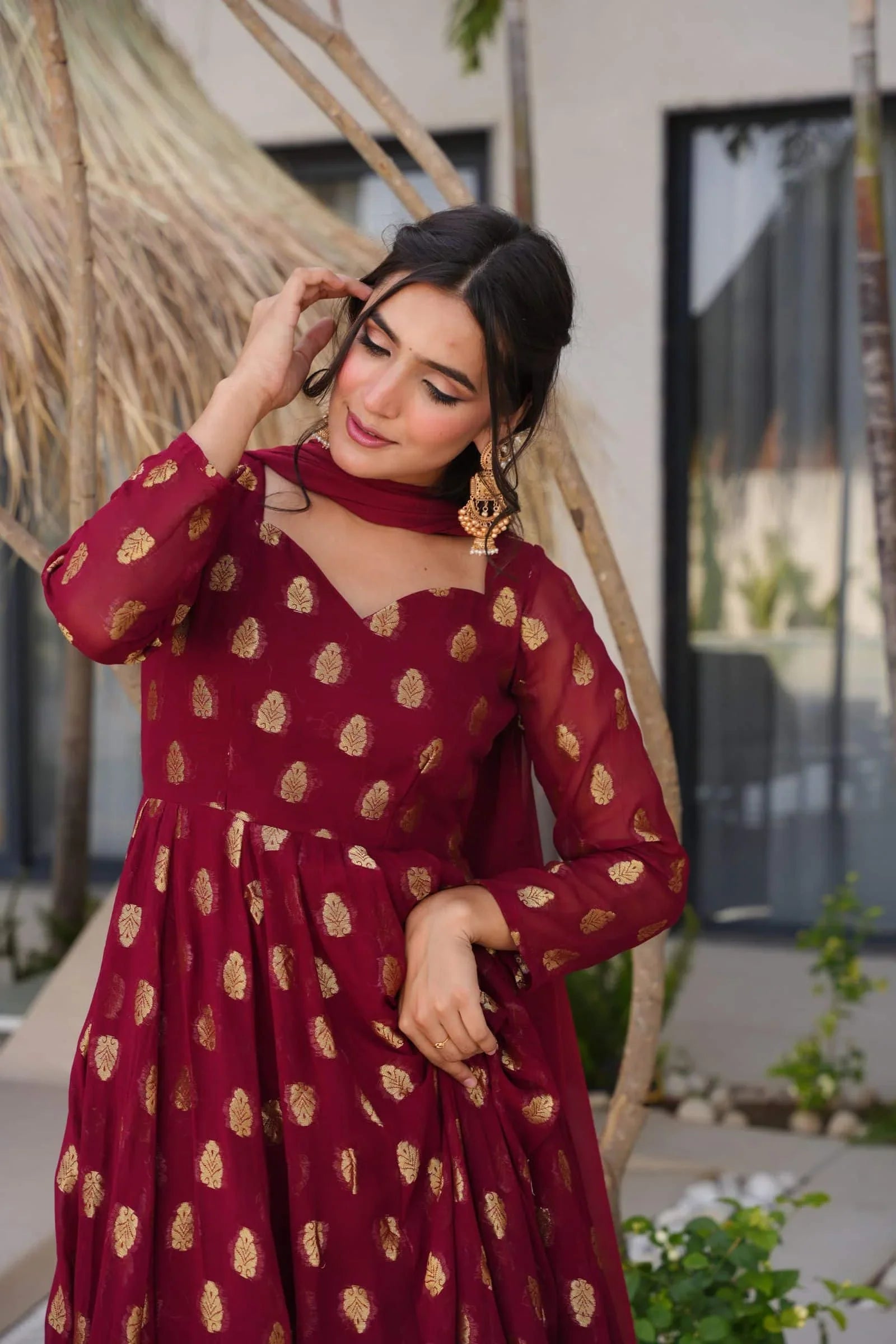 Woman wearing a maroon dress with gold patterns outdoors.
