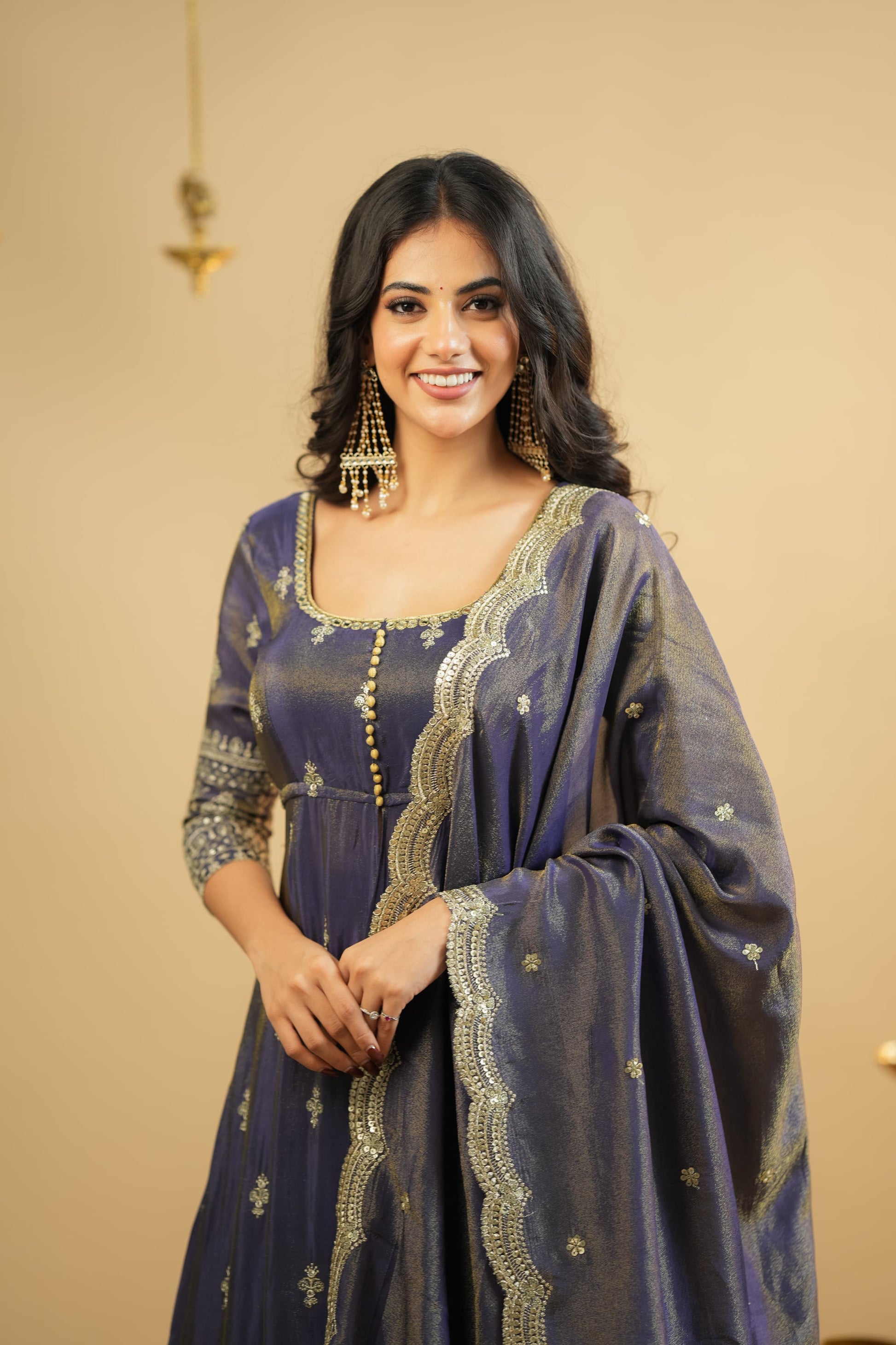 Woman wearing a blue embroidered traditional outfit against a beige background