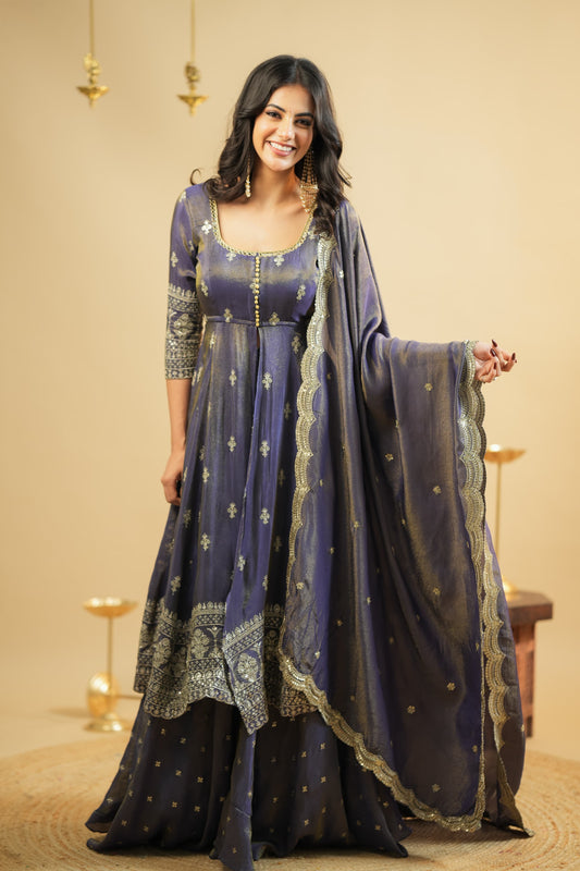 Woman wearing a traditional outfit with a long, dark blue dress and matching dupatta against a beige background.