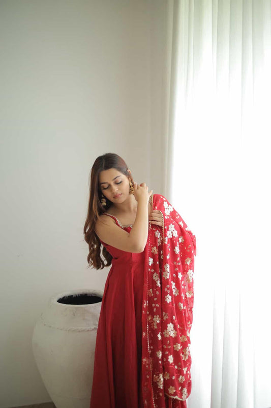 Woman in a red dress holding a red floral shawl against a white wall.