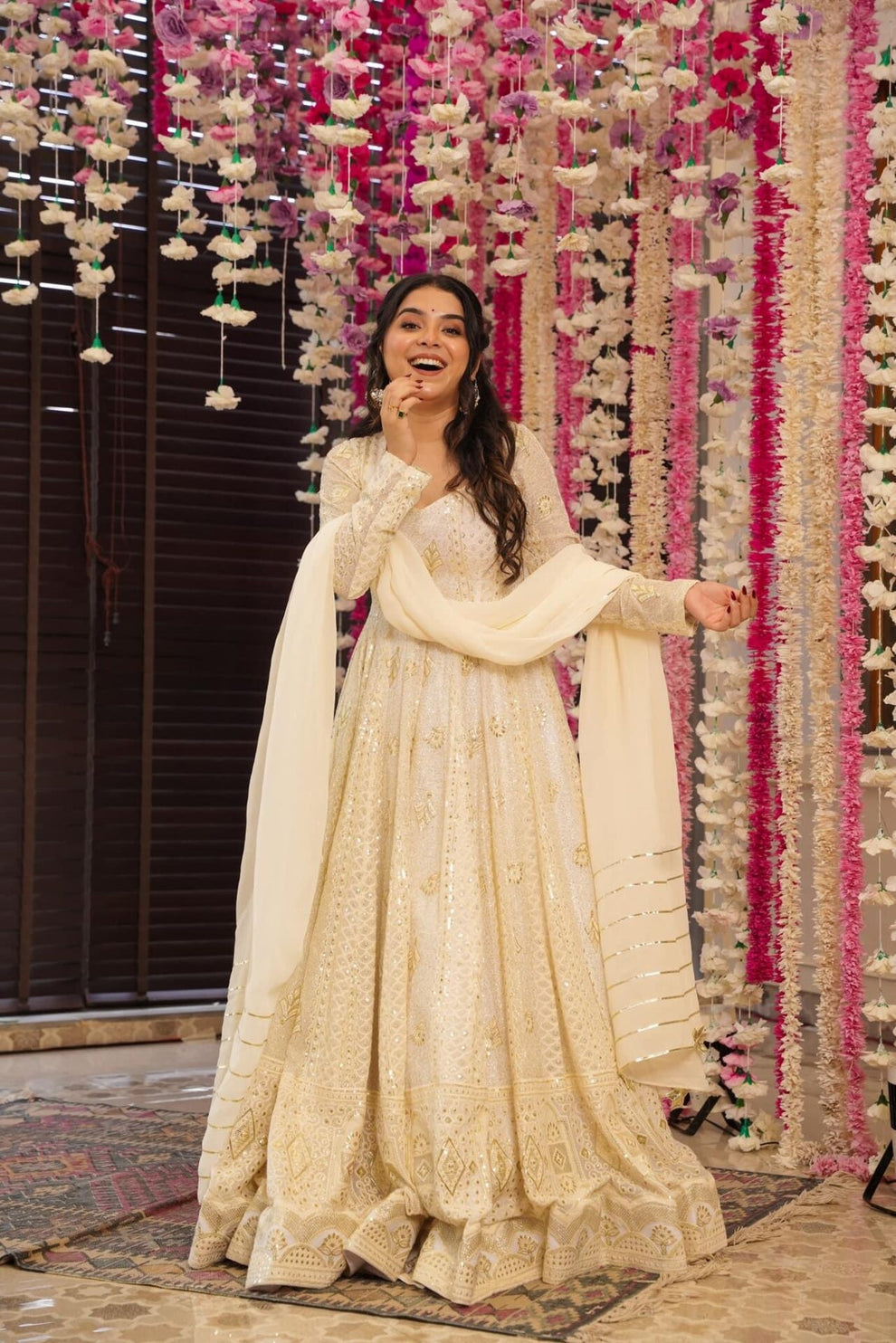 Woman in a white traditional outfit standing in front of floral decorations