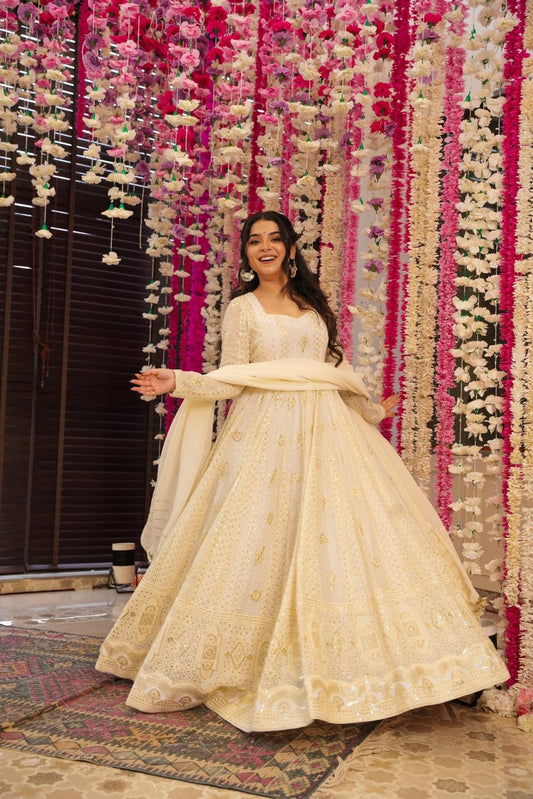 Woman in a cream traditional outfit standing in front of a decorative floral wall.