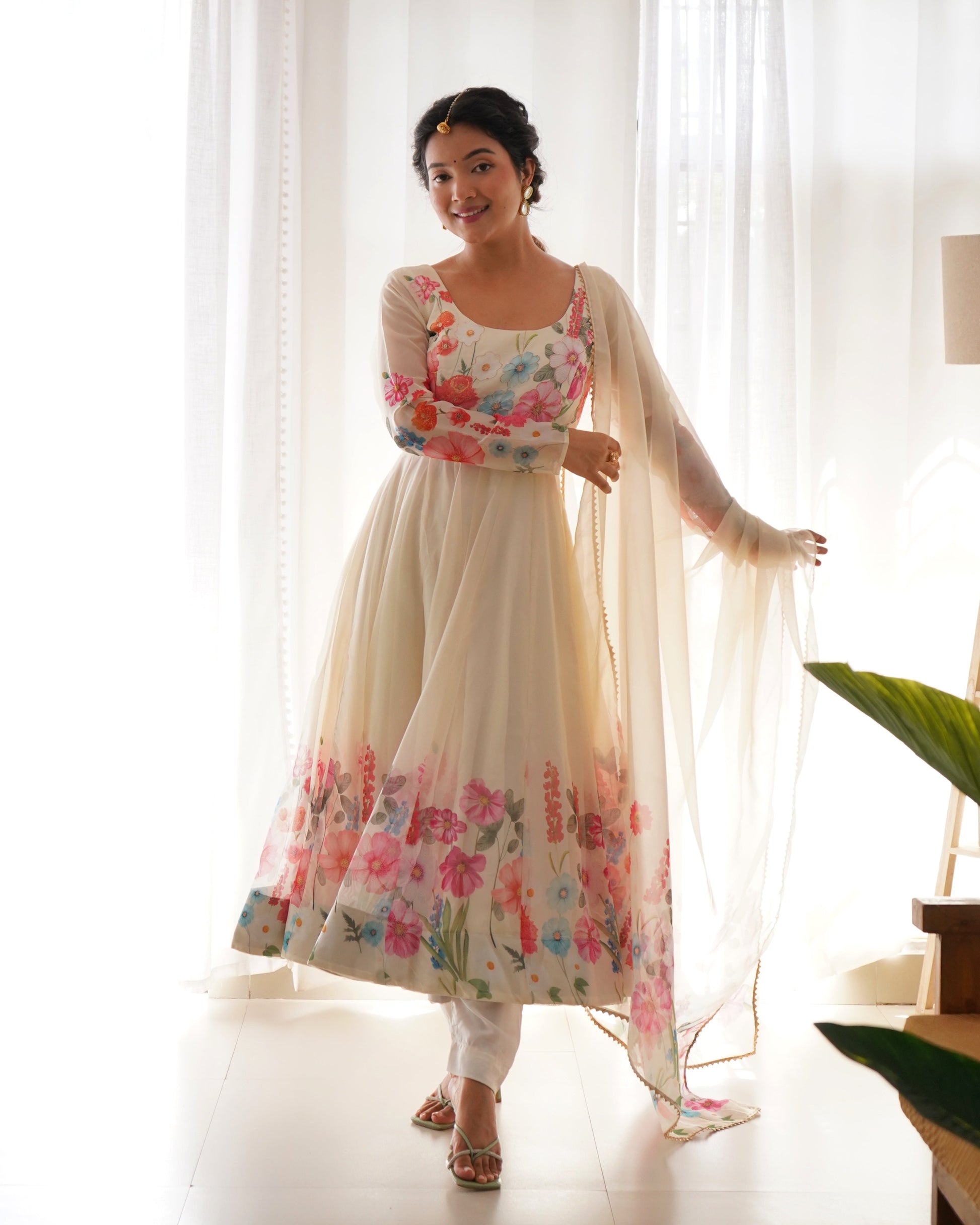 Woman wearing a floral dress with a sheer dupatta in a bright room.