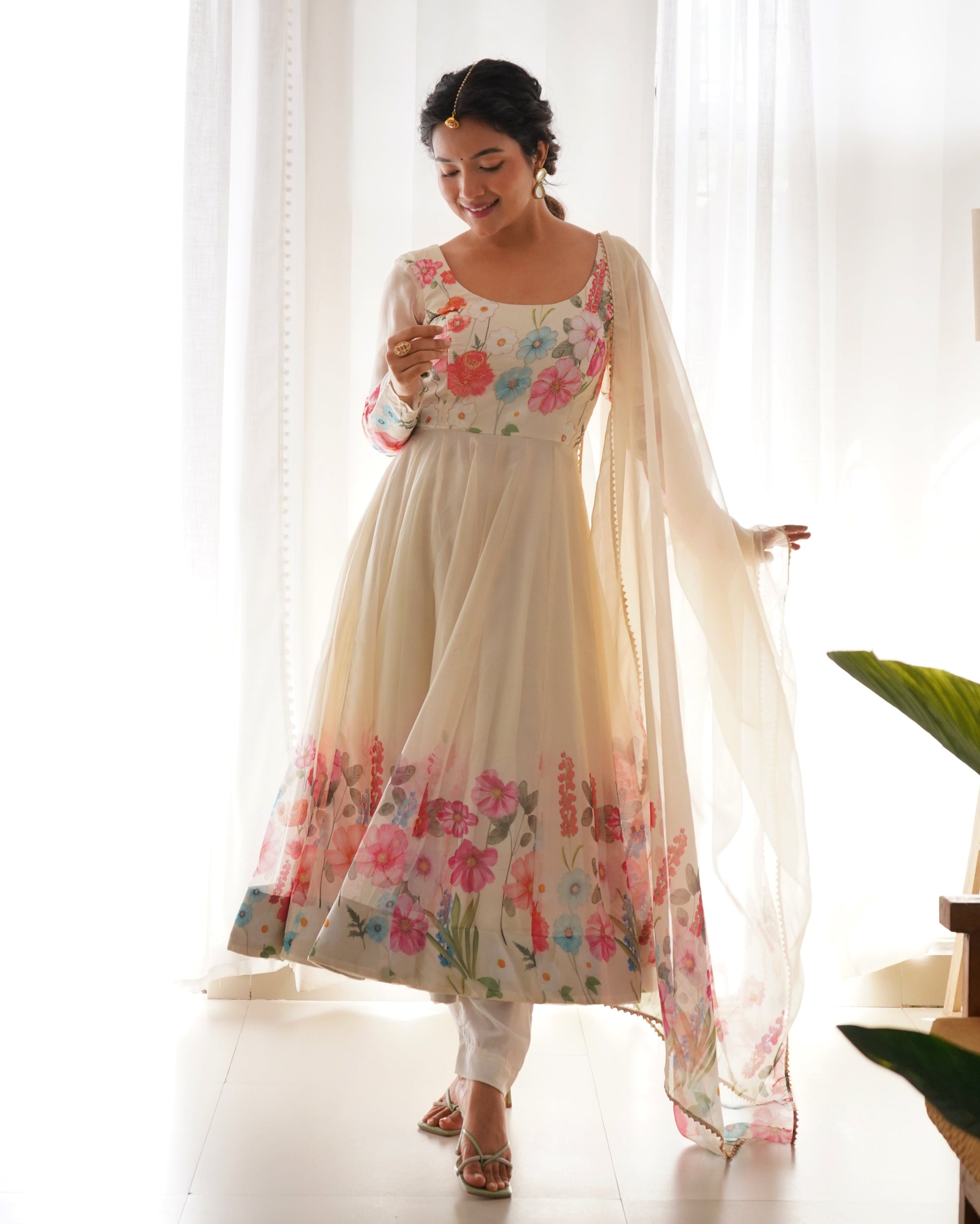 Woman wearing a floral dress with a sheer dupatta in a bright room.