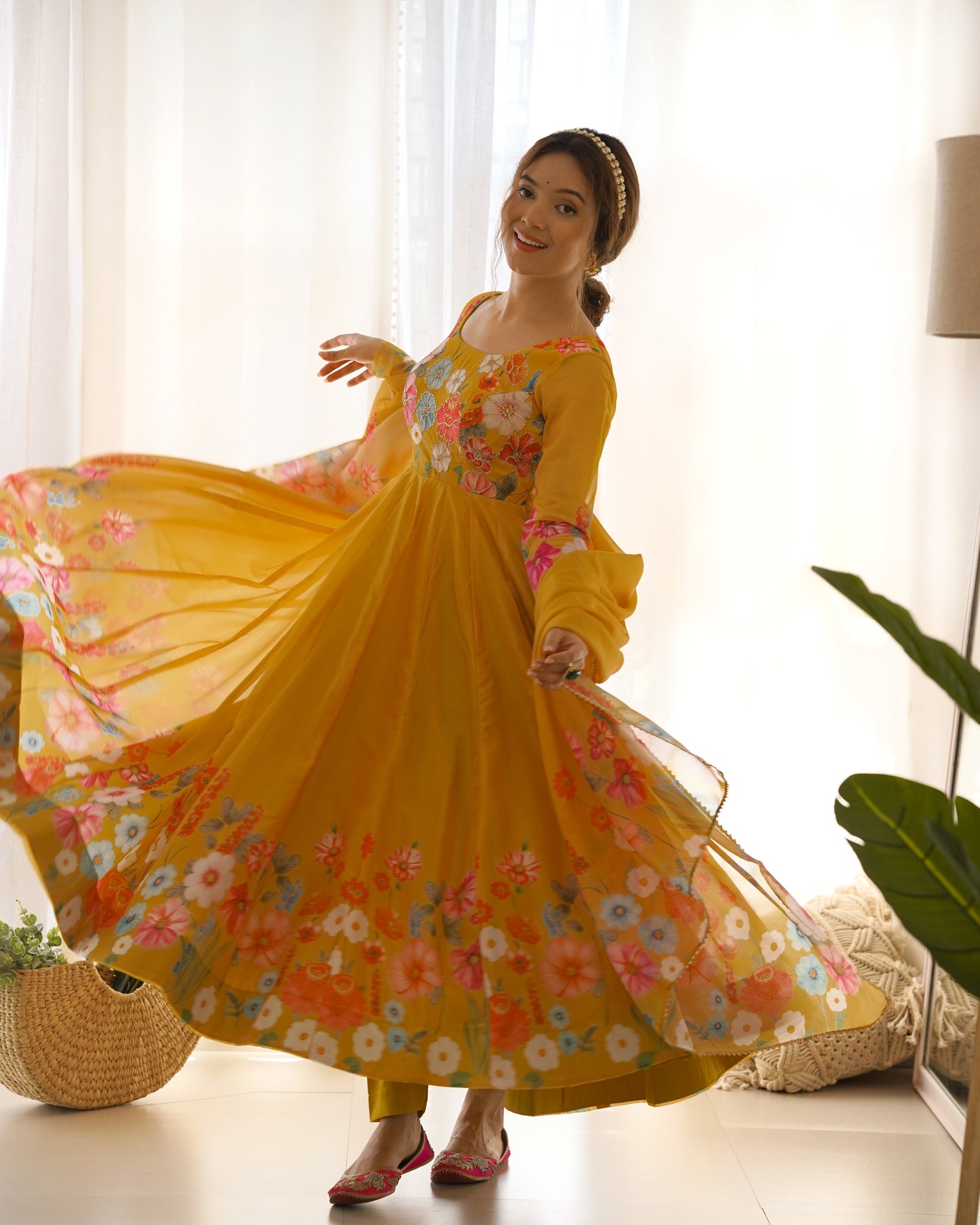 Woman in a yellow floral dress twirling in a room with white curtains and a plant.